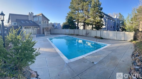 A swimming pool in a backyard surrounded by a concrete patio and a stone wall.