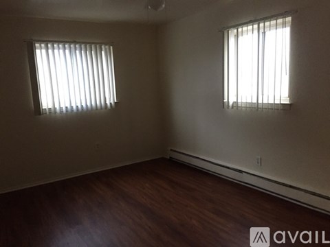 A room with wooden floors and two windows with blinds.