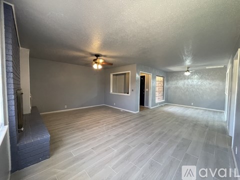 A spacious room with a ceiling fan and light, and a fireplace on the left side.