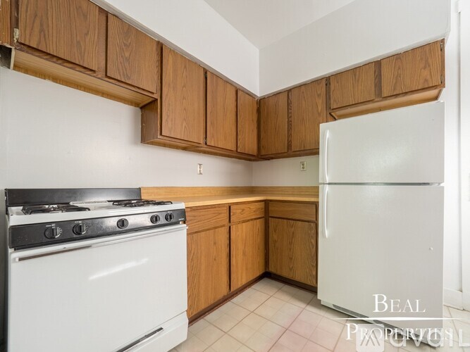 A kitchen with a white stove and a white refrigerator with wooden cabinets.