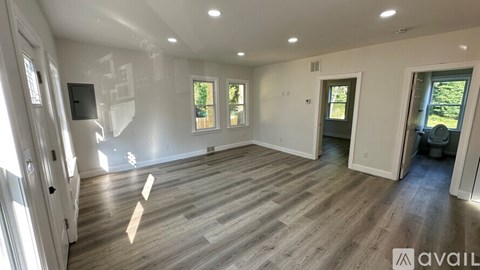 A spacious room with wooden flooring and white walls, with a door on the right side.