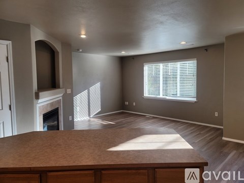A spacious living room with a fireplace and a large window with blinds.