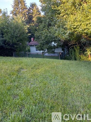 A grassy field with trees and a small building in the background.