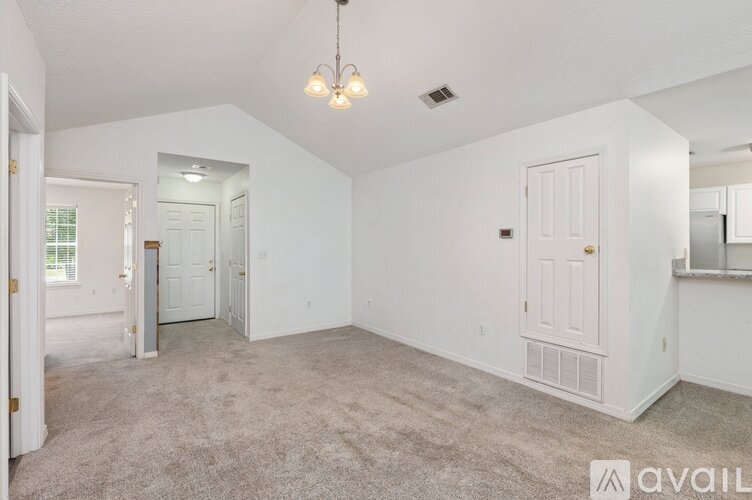 A spacious living room with a carpeted floor and a chandelier hanging from the ceiling.