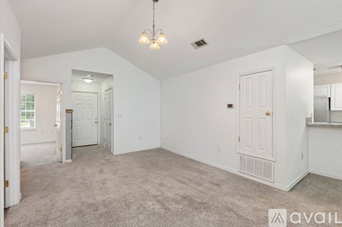 A spacious living room with a carpeted floor and a chandelier hanging from the ceiling.