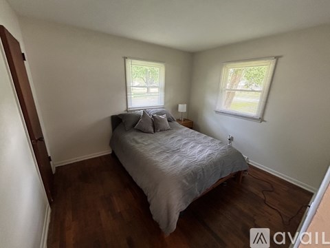 A bedroom with a bed, two windows, and a wooden floor.