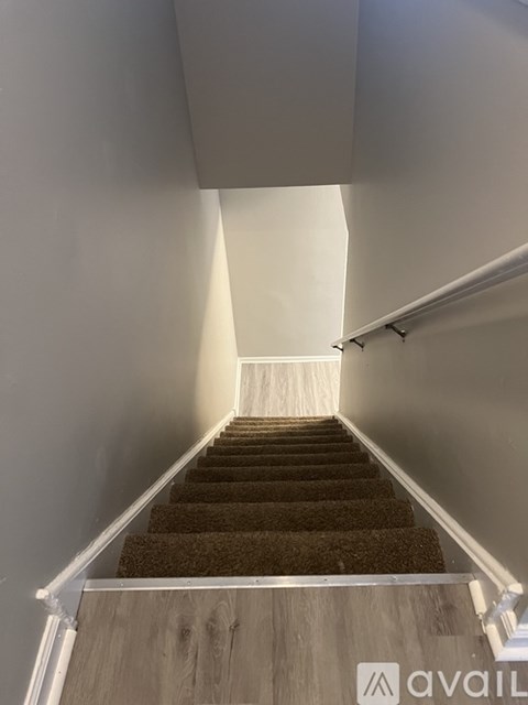 A staircase with a carpeted runner and wooden steps leading up to a white wall.
