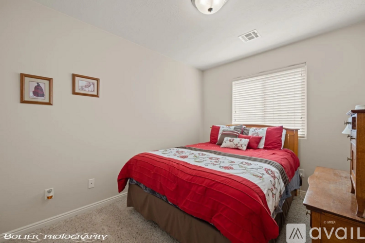 A bedroom with a red bedspread and two pictures on the wall.