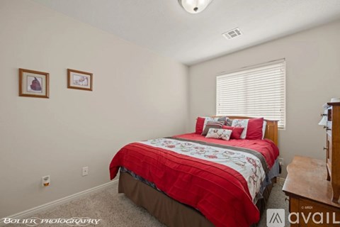 A bedroom with a red bedspread and two pictures on the wall.