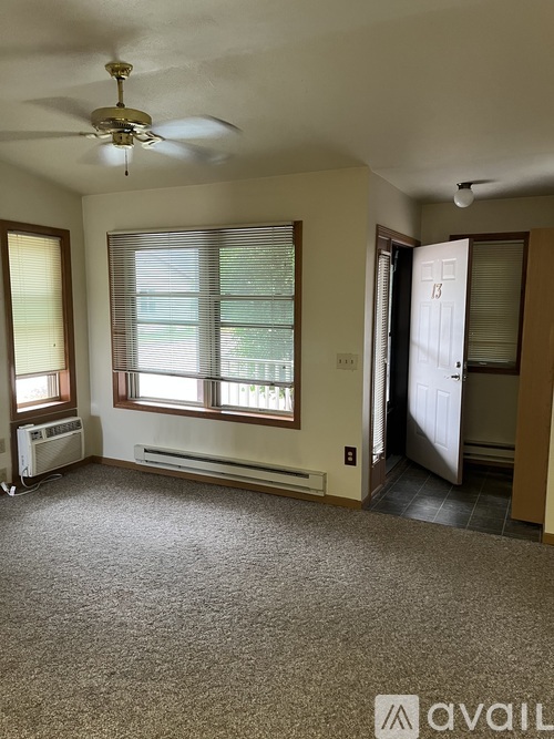A room with a carpeted floor, a ceiling fan, and a window with blinds.