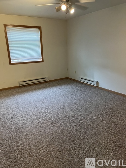 A room with a carpeted floor, a window with blinds, and a ceiling fan.