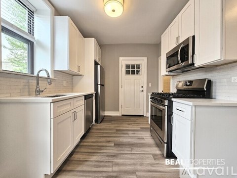 A kitchen with white cabinets and appliances, a sink, and a door in the background.