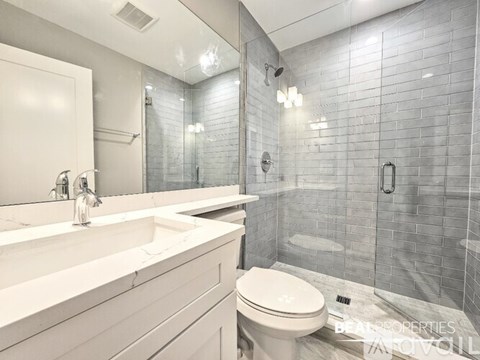 A white toilet sits in a bathroom with a grey tiled shower.