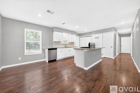 A spacious kitchen with white cabinets and a wooden floor.