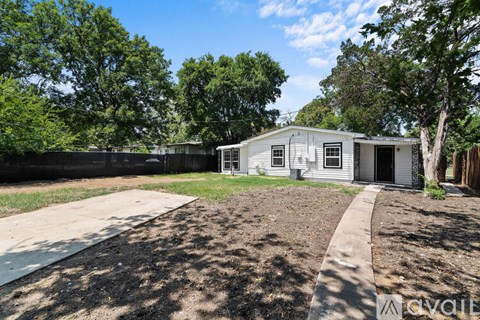 A mobile home sits in a grassy backyard with a sidewalk leading to the front door.