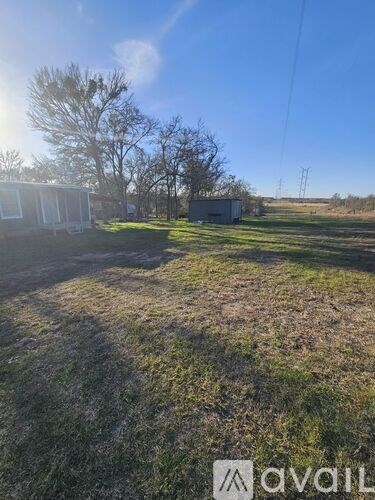 A grassy field with a house and trees in the background.