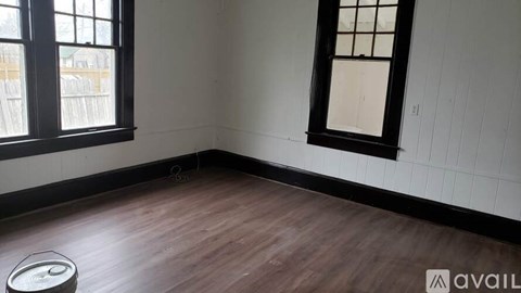A room with wooden flooring and two windows.