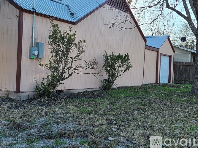 A house with a brown siding and a blue roof with a small tree in front.