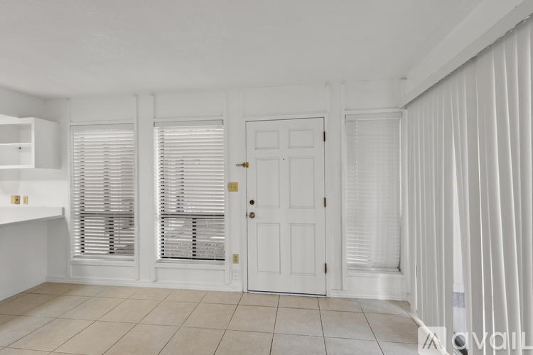 A white room with a door, windows with blinds, and a tiled floor.
