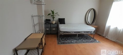 A bedroom with a bed, a mirror, a plant, and a desk.