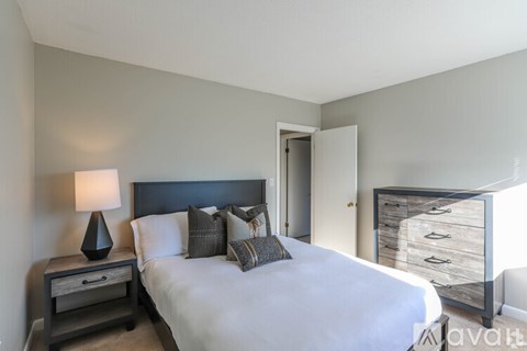 A bedroom with a large bed, a nightstand with a lamp, and a dresser with a mirror.