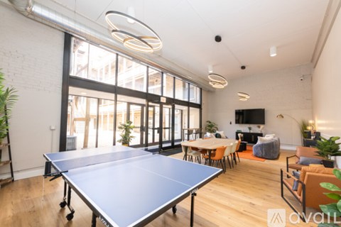 A ping pong table is in the middle of a room with a white brick wall and a large window.