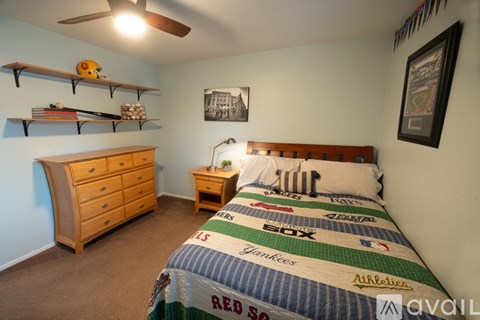 A bedroom with a bed covered in a quilt with multiple team logos on it.