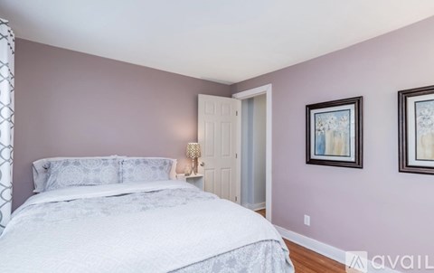 A bedroom with a bed, two pictures on the wall, and a lamp on a side table.