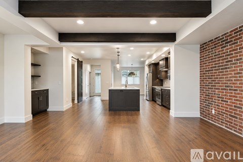 A spacious living room with a brick wall on one side and a kitchen area with a refrigerator and cabinets.