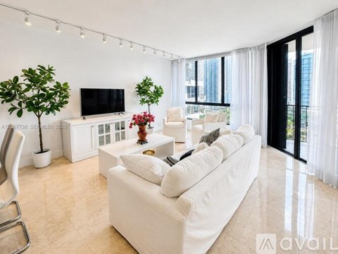 A living room with a white couch, television, and a plant.