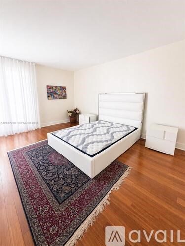 A bedroom with a white bed and a rug on the floor.