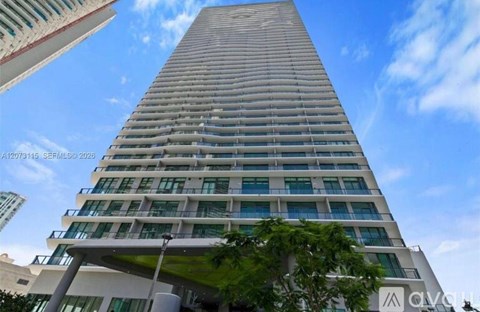 A tall building with many windows and balconies is seen against a blue sky.