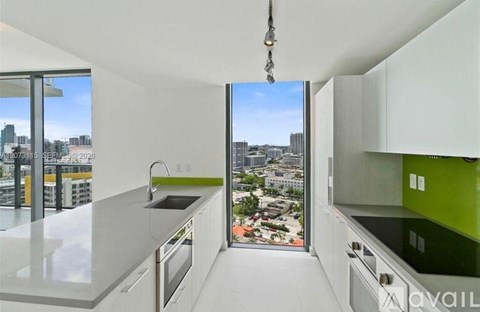 A kitchen with white cabinets and a green backsplash with a view of the city outside the window.