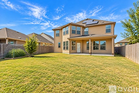 A house with a brown roof and tan walls is surrounded by a fence and has a green lawn.