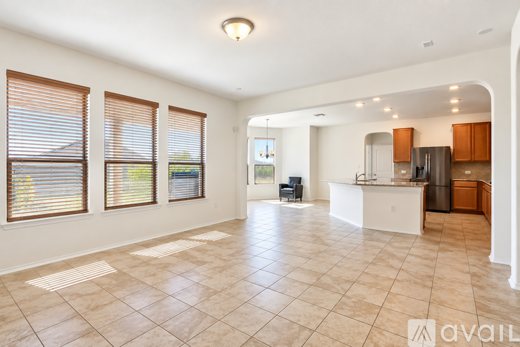 A spacious living room with tiled flooring and a kitchen area in the background.