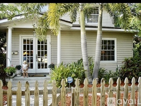 A house with a white fence and a woman sitting on the porch.