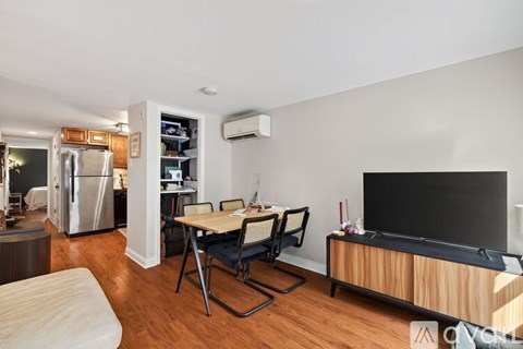 A living room with a television, a table and chairs, and a refrigerator in the kitchen area.