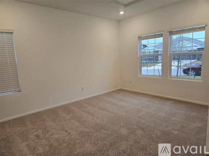 A room with a carpeted floor, a window, and a view of a house and trees outside.
