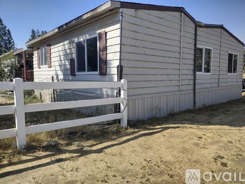 A white fence surrounds a small house with a brown roof.