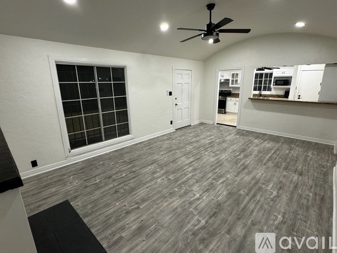 A room with a ceiling fan and a window with a view of a kitchen.