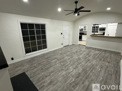A room with a ceiling fan and a window with a view of a kitchen.