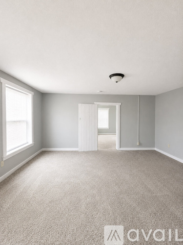 A spacious room with a carpeted floor and a window on the left side.