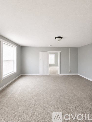 A spacious room with a carpeted floor and a window on the left side.