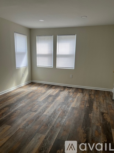A room with wooden flooring and two windows.