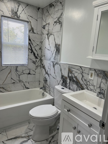 A white toilet sits next to a bathtub in a bathroom with marble tiles.