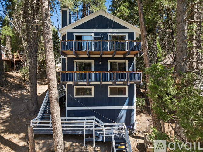 A blue house with a balcony is surrounded by trees.