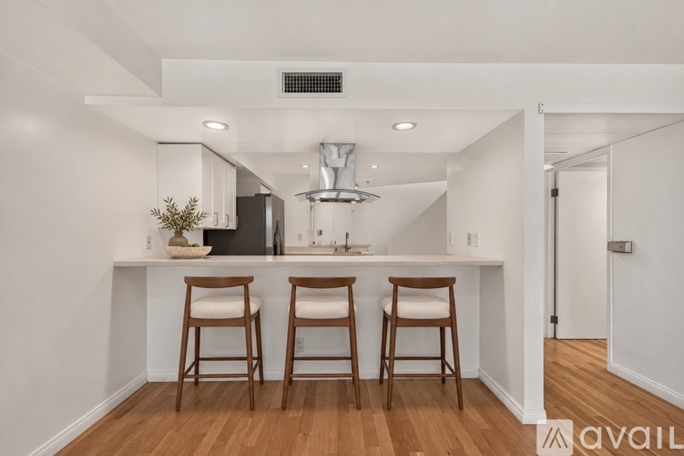A kitchen with white walls and wooden floors has a bar area with two stools.