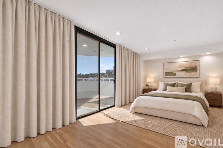 A bedroom with a large bed and a view of the outside through a glass door.