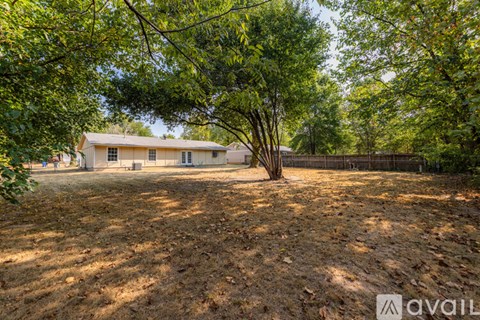 A house is surrounded by trees and has a fence in front of it.