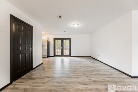 A spacious room with wooden flooring and a large black door.